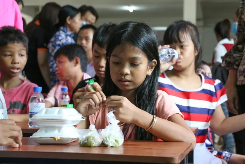 Children sit together around a table sharing a meal.